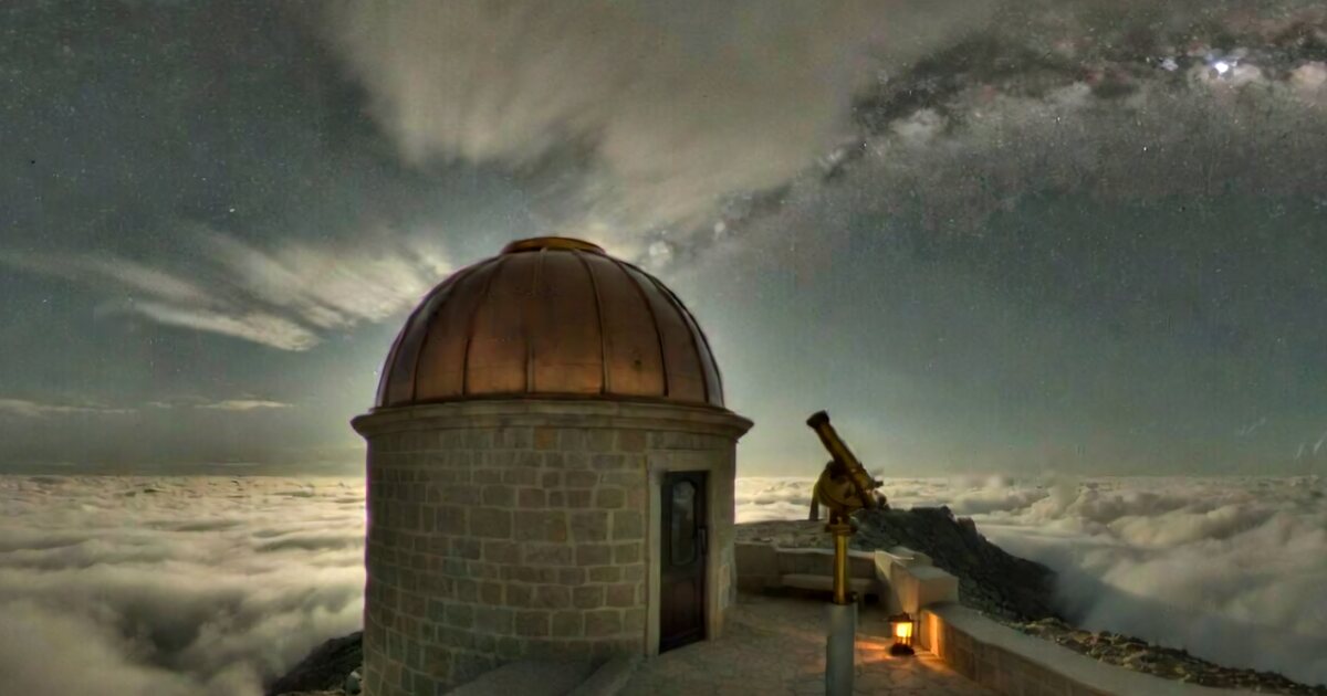 A copper-domed stone observatory and a brass telescope on a mountain top above a sea of clouds, under the Milky Way at night.