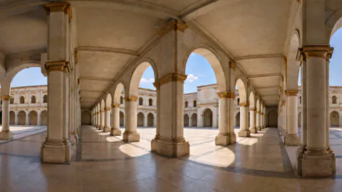 A sunlit cloister walk of white arches around a stone courtyard.